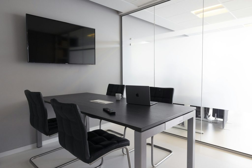 Sala de reunião moderna com parede de vidro, mesa escura e notebook