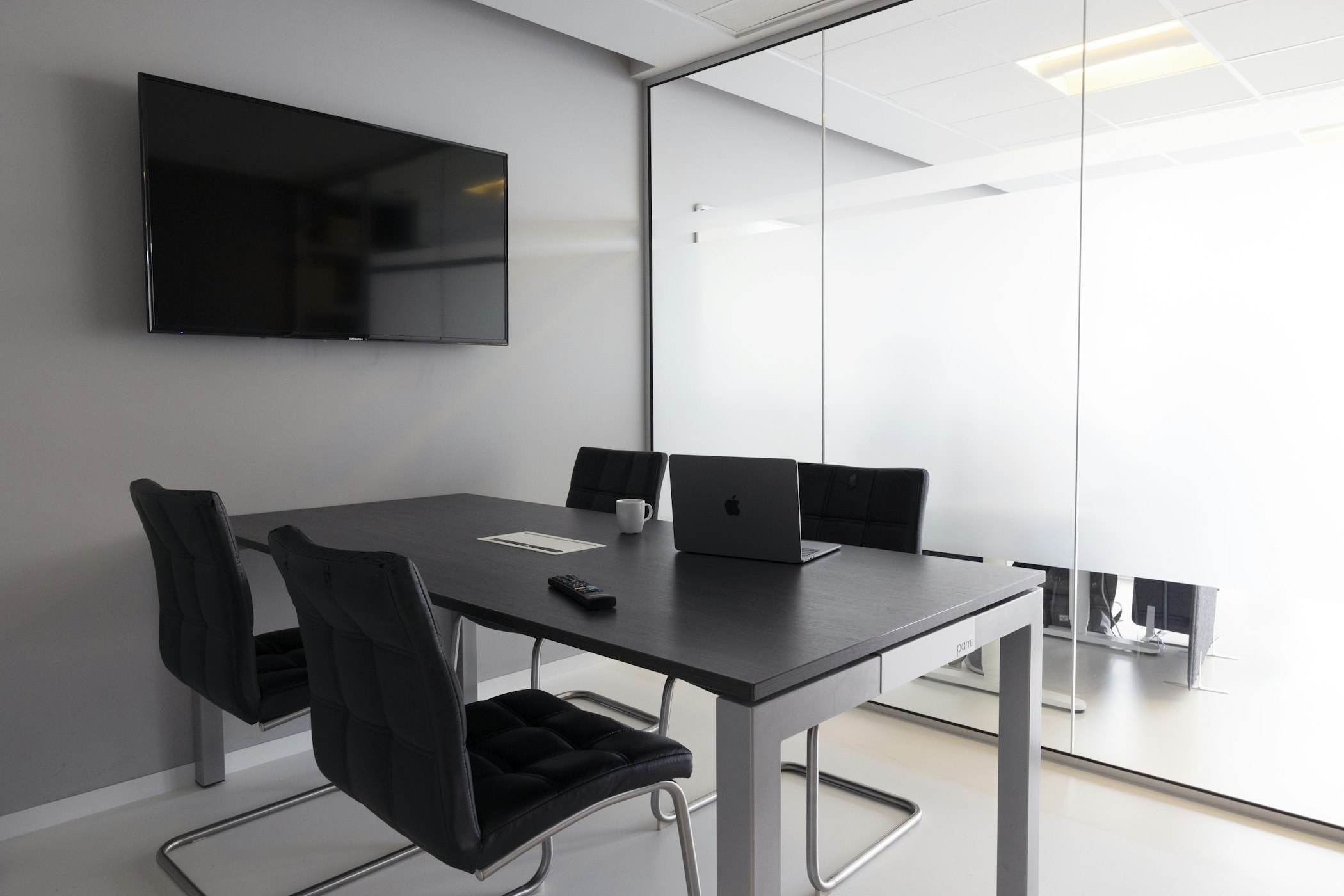 Sala de reunião moderna com parede de vidro, mesa escura e notebook