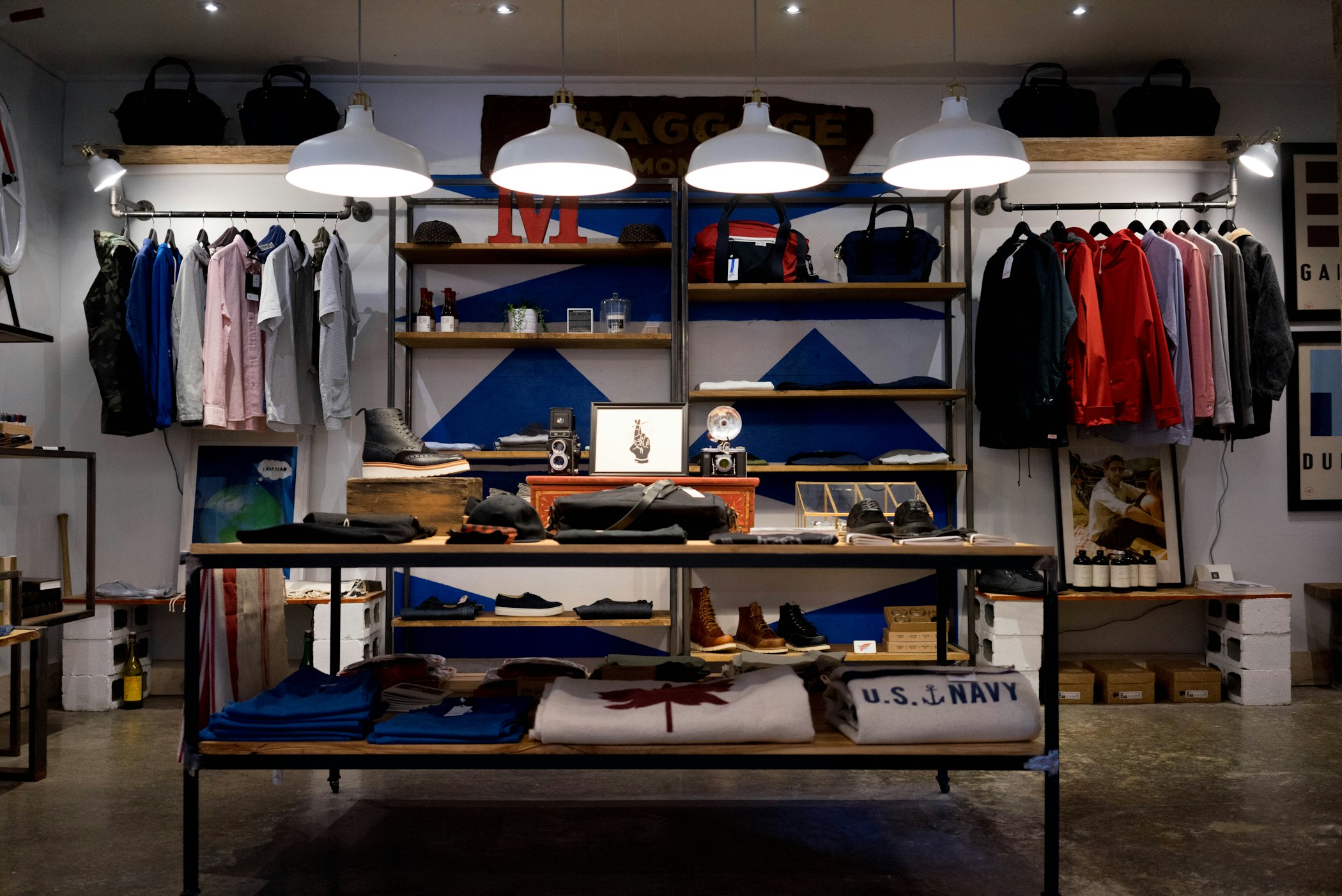 Interior de uma pequena loja de roupas com araras, prateleiras e luminárias