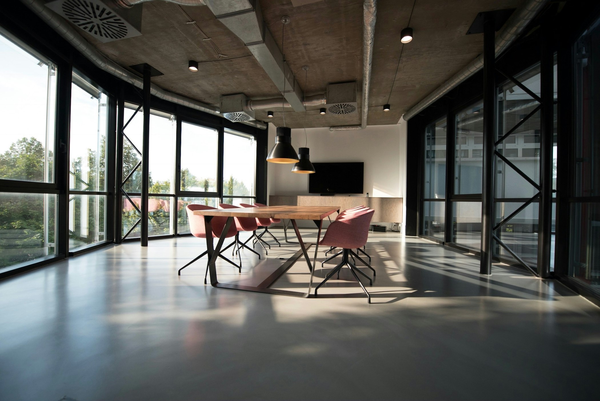 Sala de reunião ampla em um escritório moderno, com janelas de vidro e mesa de madeira